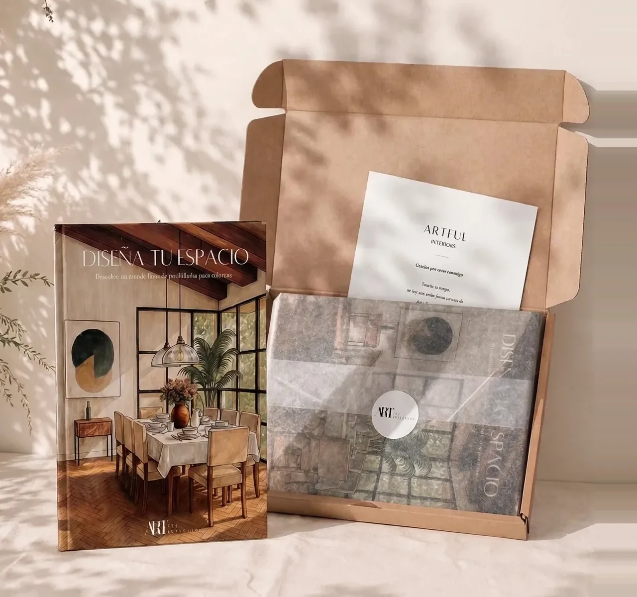 El libro Diseña tu Espacio junto a su paquete de envío abierto, con papel de seda y el sticker de Artful Interiors